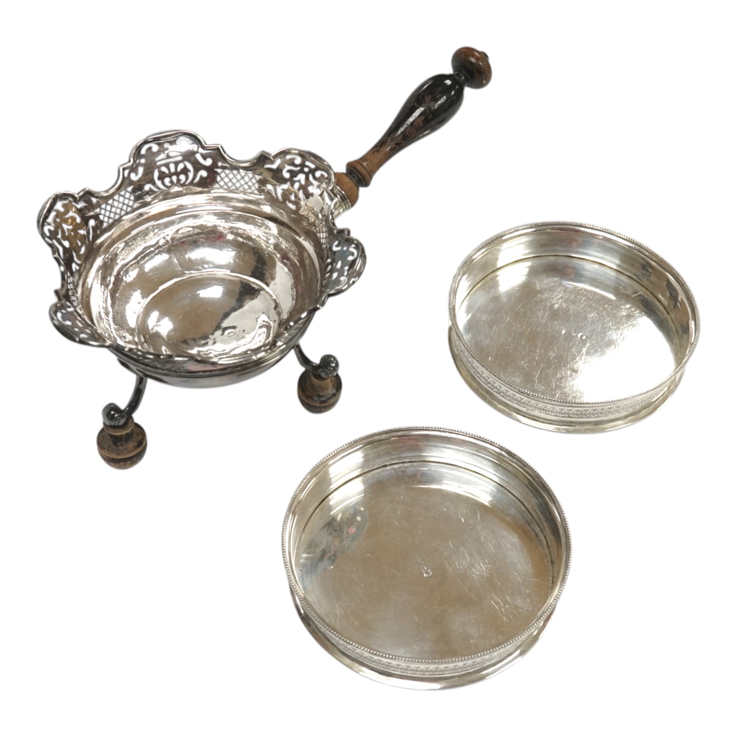 An early 19th century Dutch white metal bowl, with pierced border and turned wooden handle, length 27cm, (a.f.), together with a pair of continental white metal mounted wine coasters, diameter 12.7cm. Condition - poor to